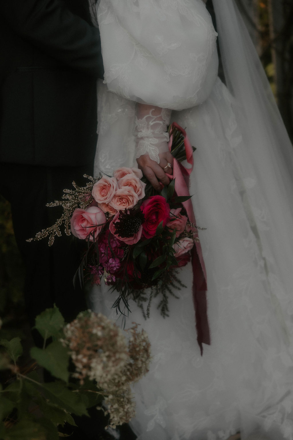 Romantic red and pink bridal bouquet of roses and dahlias with trailing ribbons held by bride.