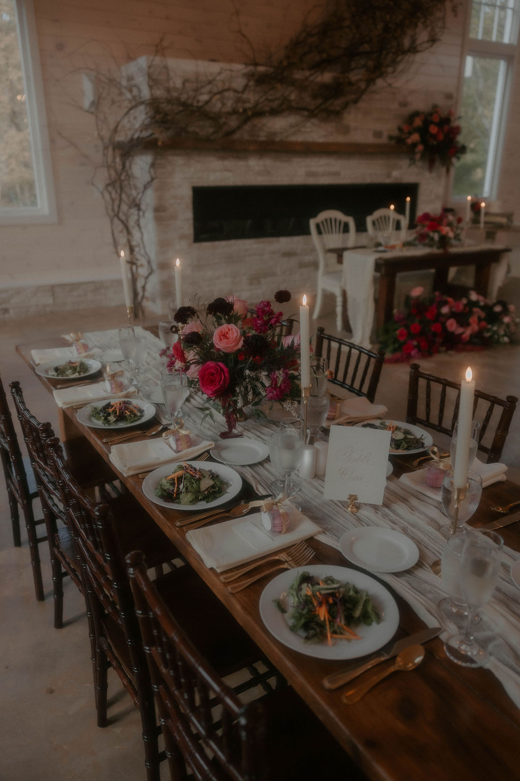 Romantic guest table at wedding reception with pink and red floral centerpiece.