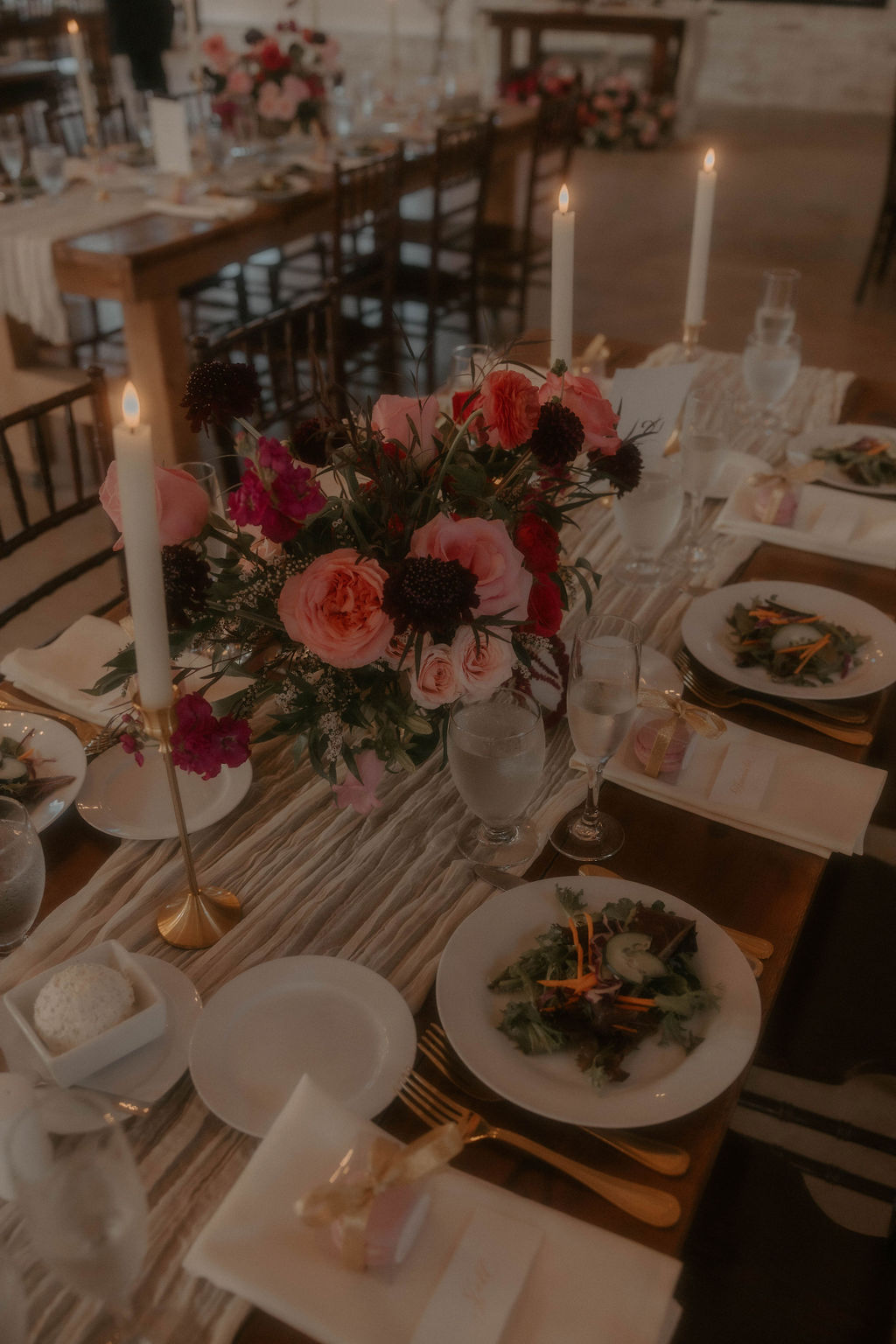 Romantic red and pink floral centerpiece with roses, scabiosa, and ranunculus on reception table at the Promise Gardens.