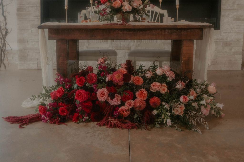 Sweetheart table floral installation in romantic red and pink palette at base of couple's table.