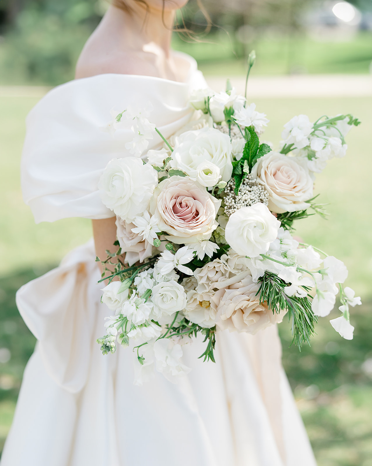 Detail of bridal bouquet in a white and blush palette with roses, ranunculus, sweet peas, rosemary, and stock.