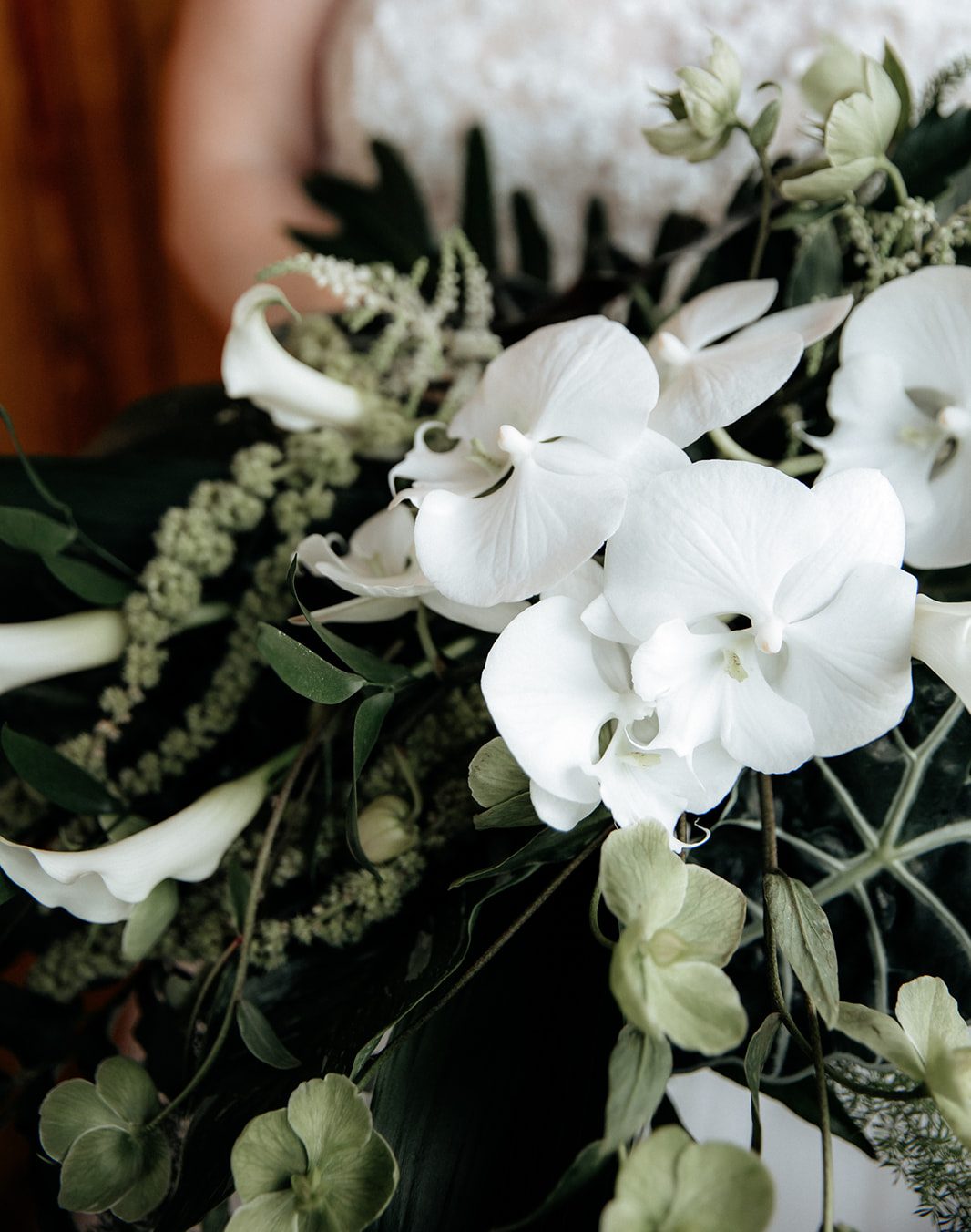 Close-up of a bouquet featuring white orchids, green hellebore, and various tropical foliage.