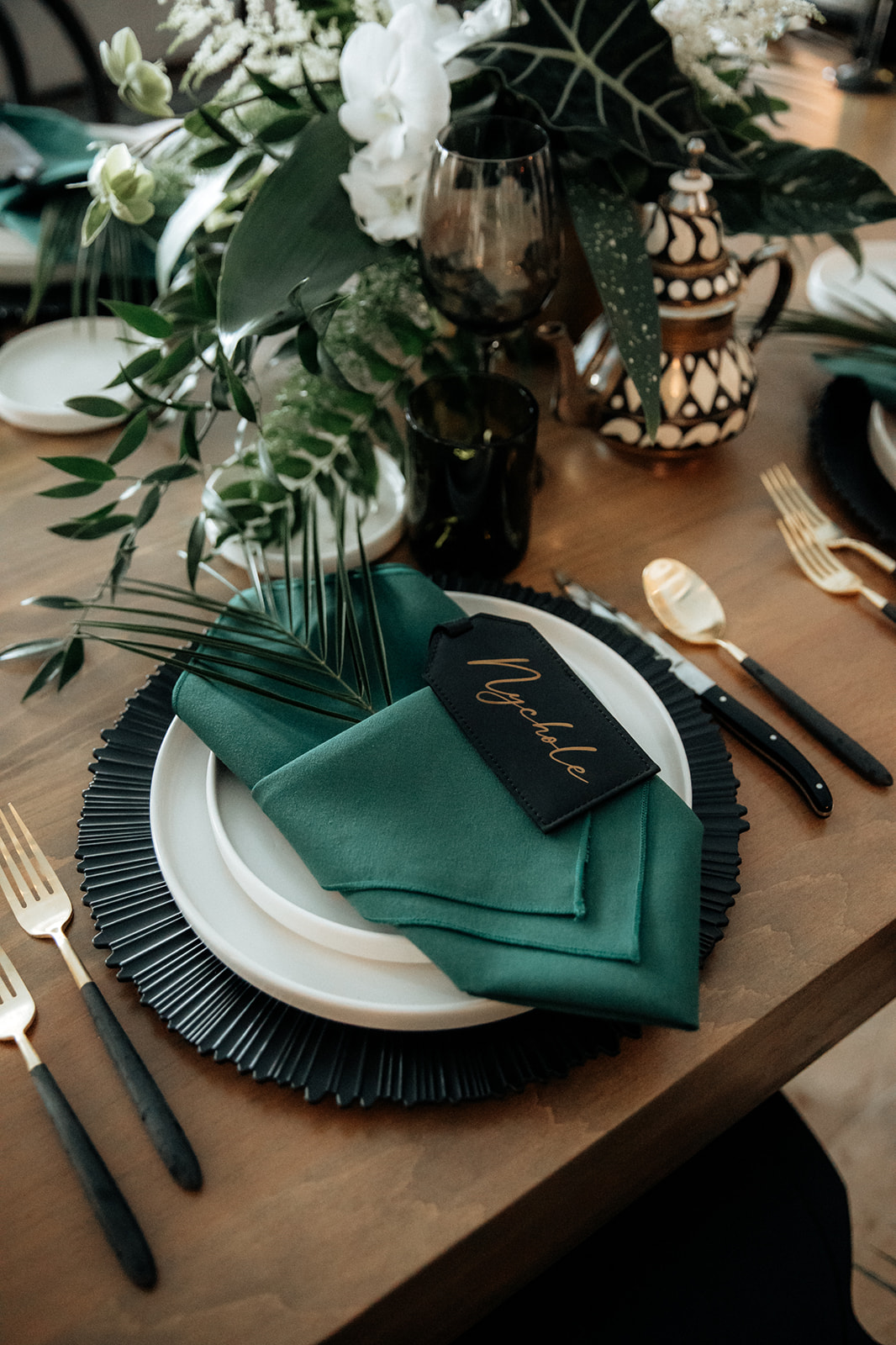 Wedding guest table setting detail with deep greens, charcoal, and tropical foliage.