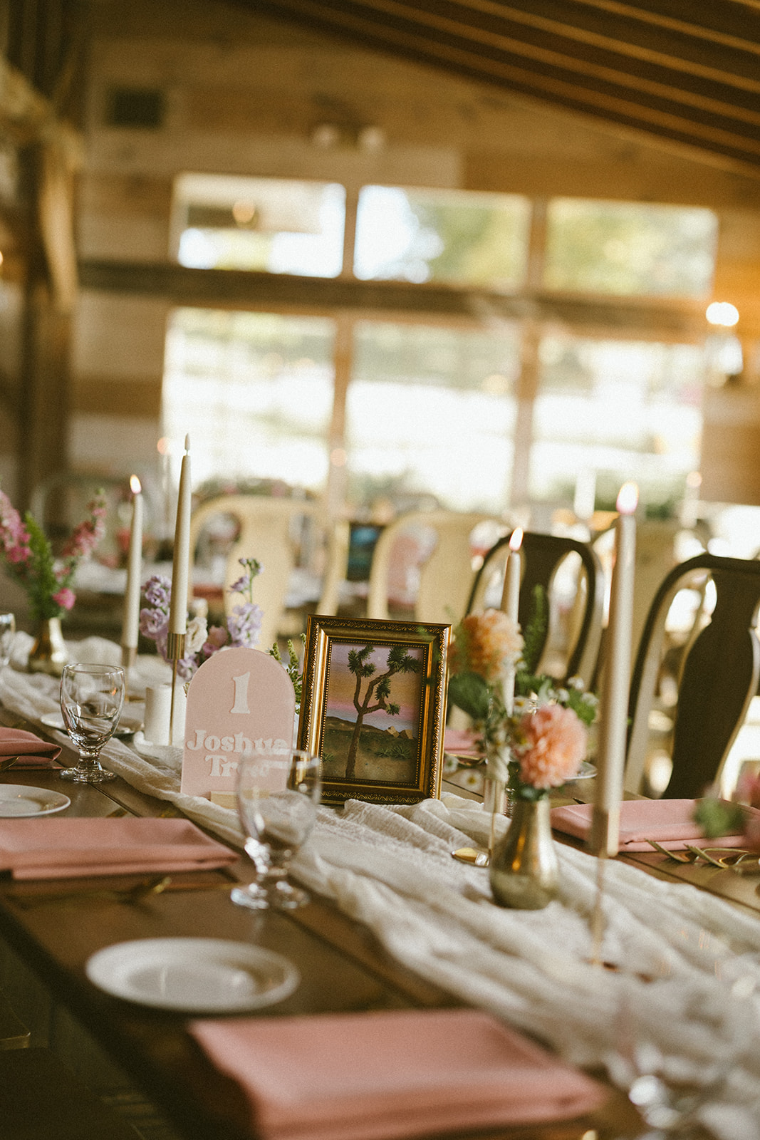 Reception guest table with candles and gold bud vases with florals in sunset palette.
