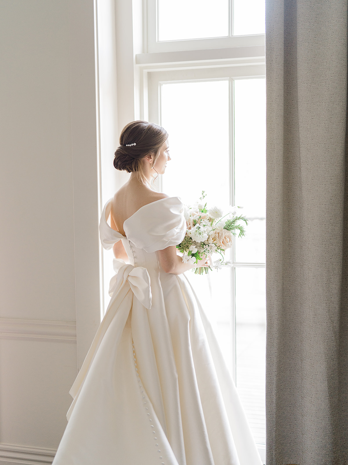 Bride standing in front of window holding a bridal bouquet in blush and white.