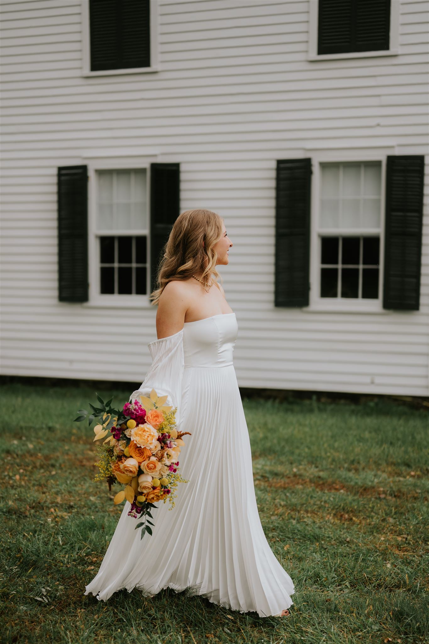 A bride walking outdoors with a bouquet in warm oranges, yellows, and magenta.