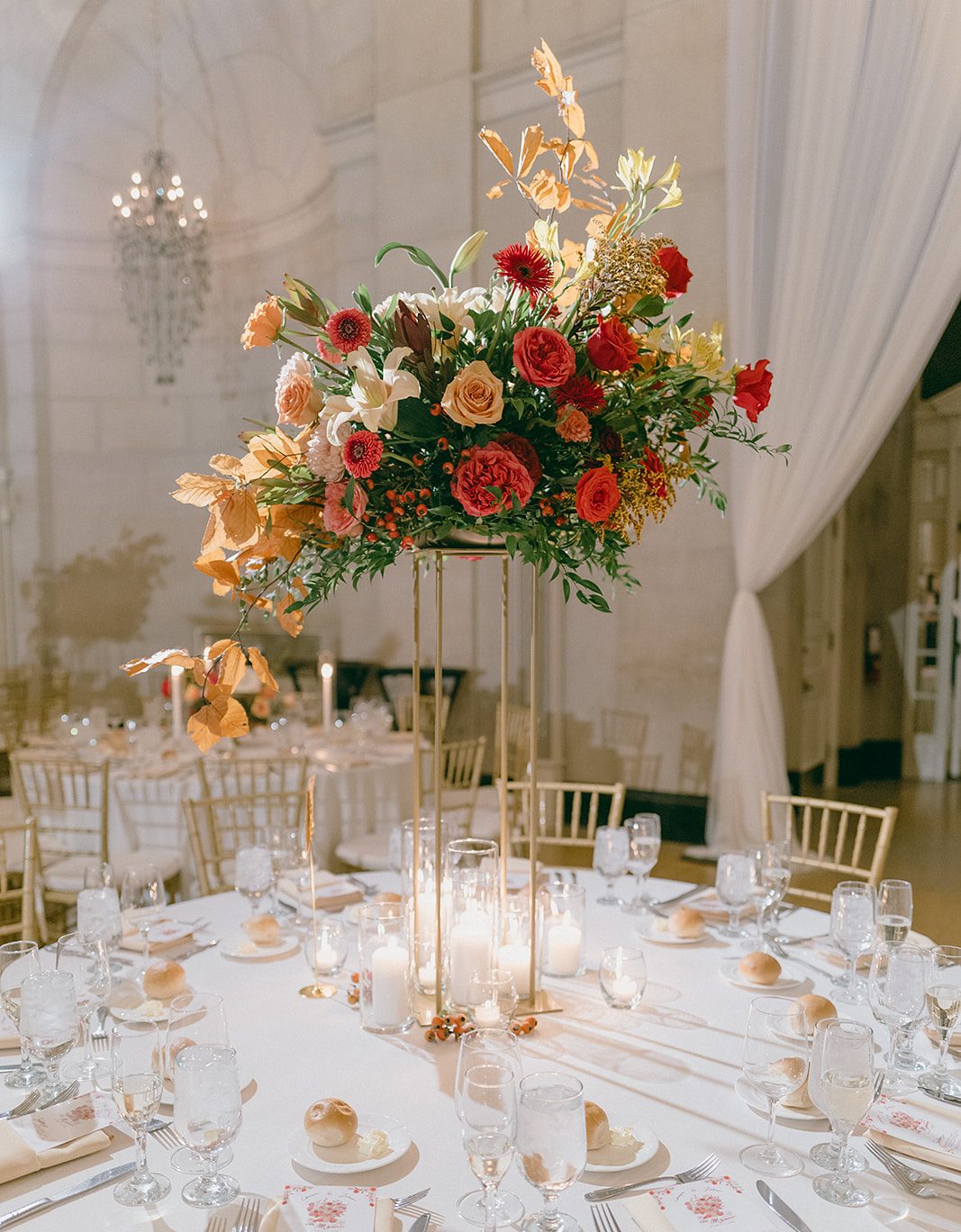 Tall elevated fall floral centerpiece on wedding reception table.