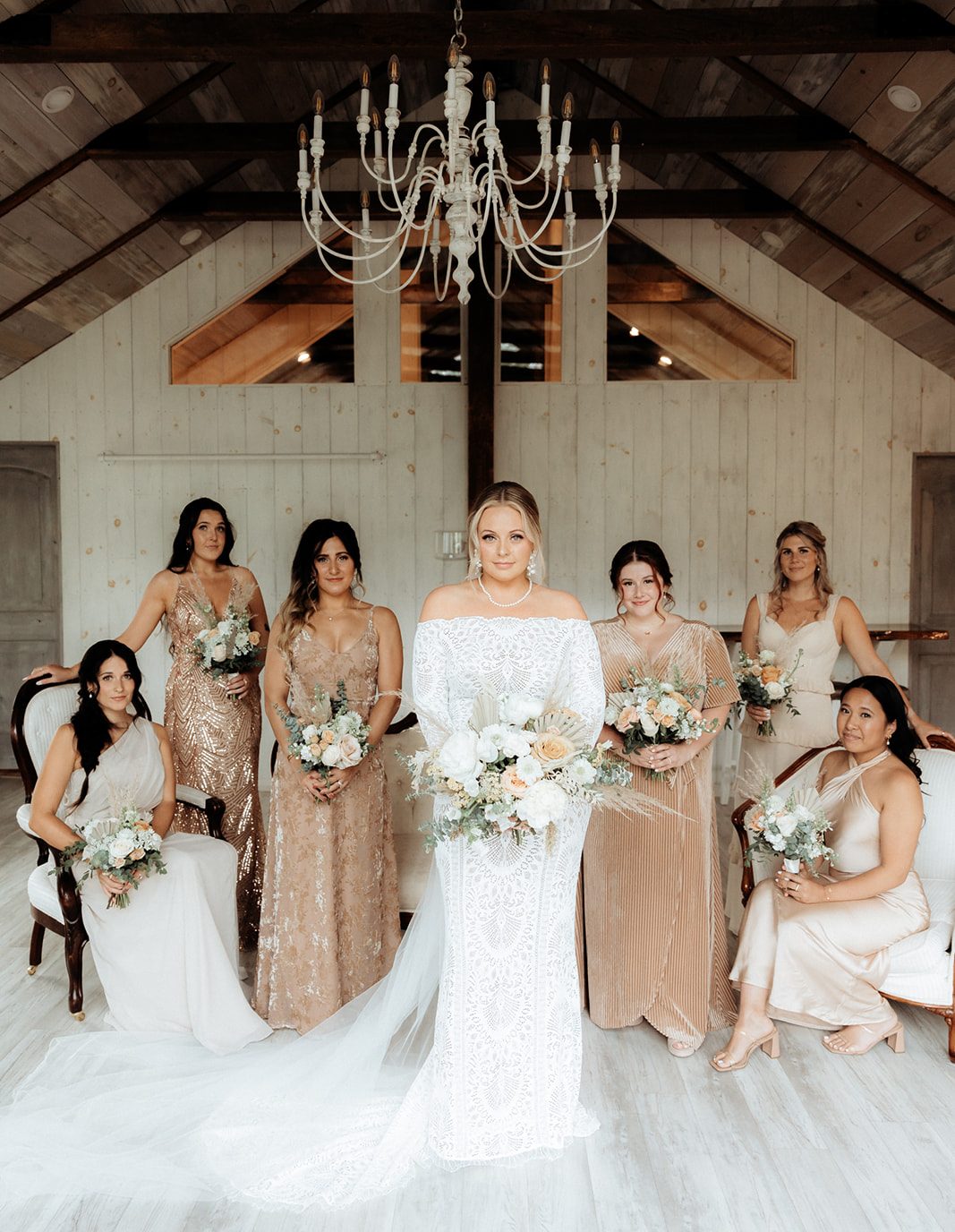Bride with bridesmaids holding flower bouquets in neutral tones in bridal suite.