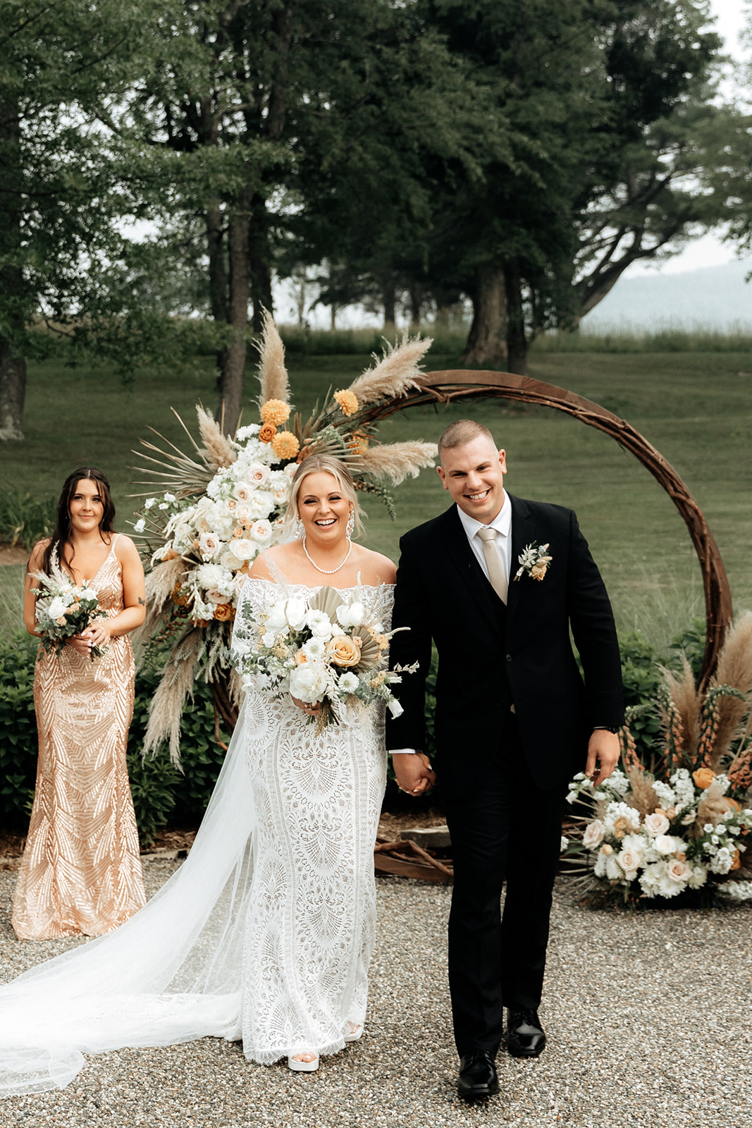 Bride and groom at wedding ceremony in front of round arbor featuring floral installations in a boho neutral style.