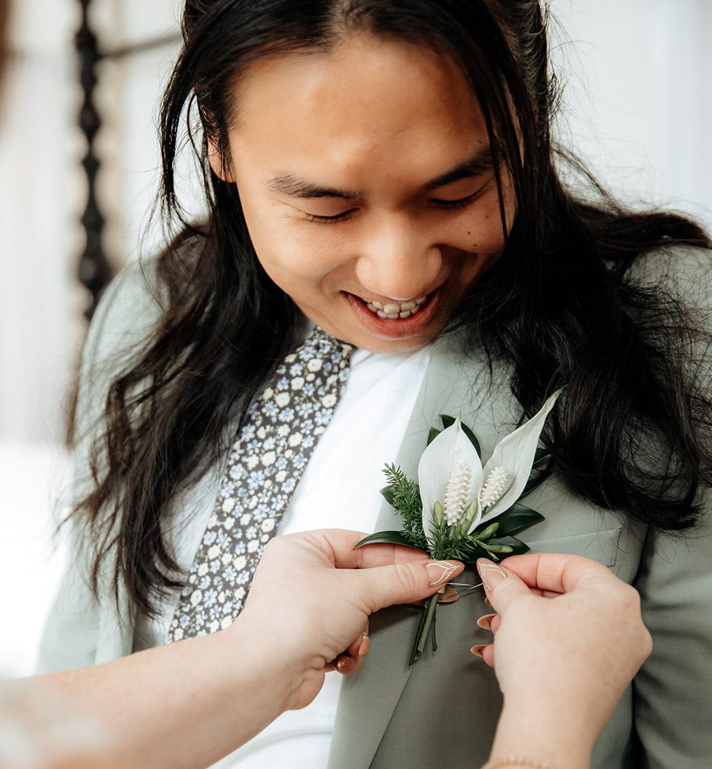 Sculptural boutonniere of white peace lily blooms pinned on groomsman.