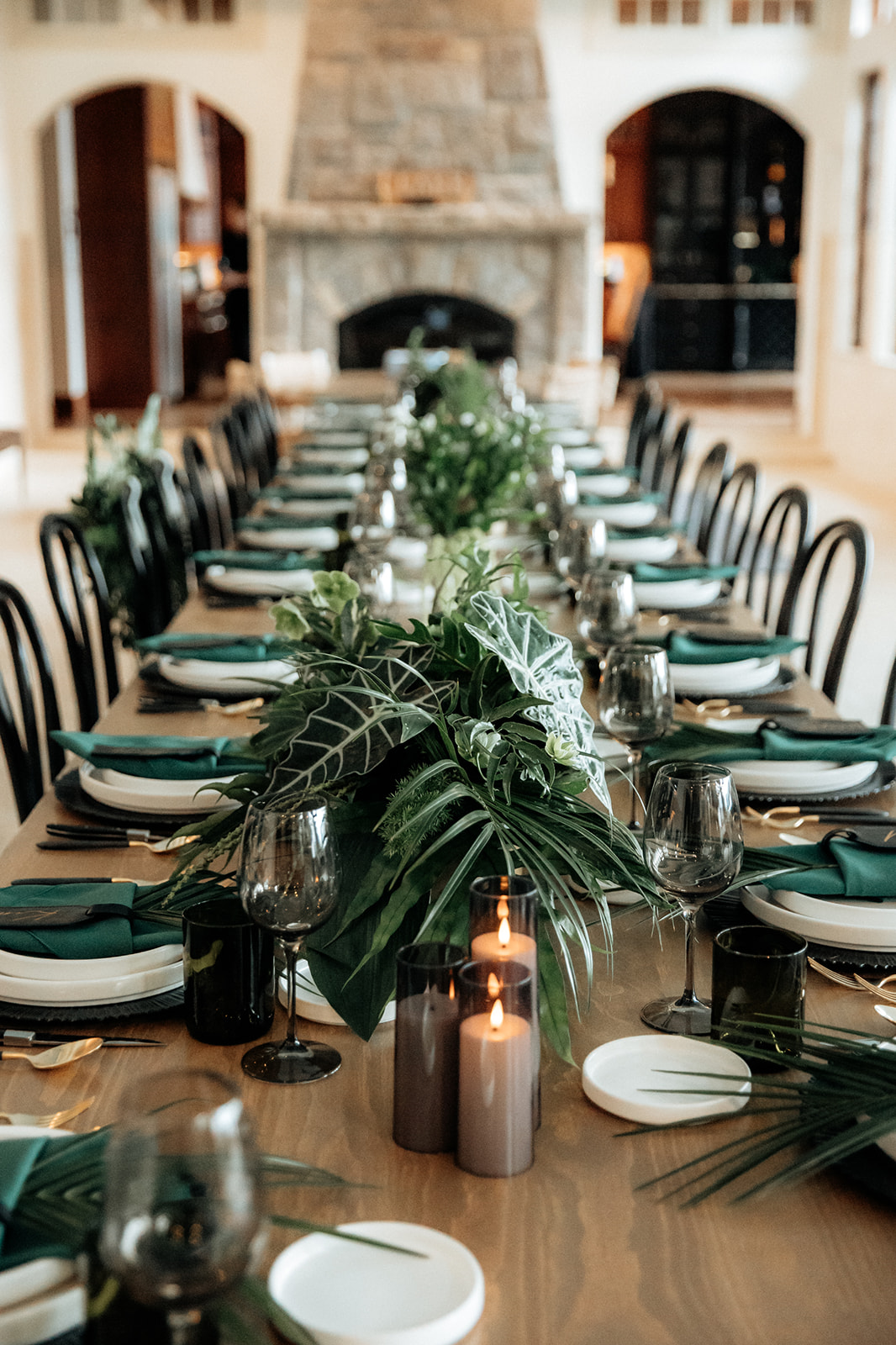 Elongated wedding reception guest table with centerpieces of dark green tropical foliage.
