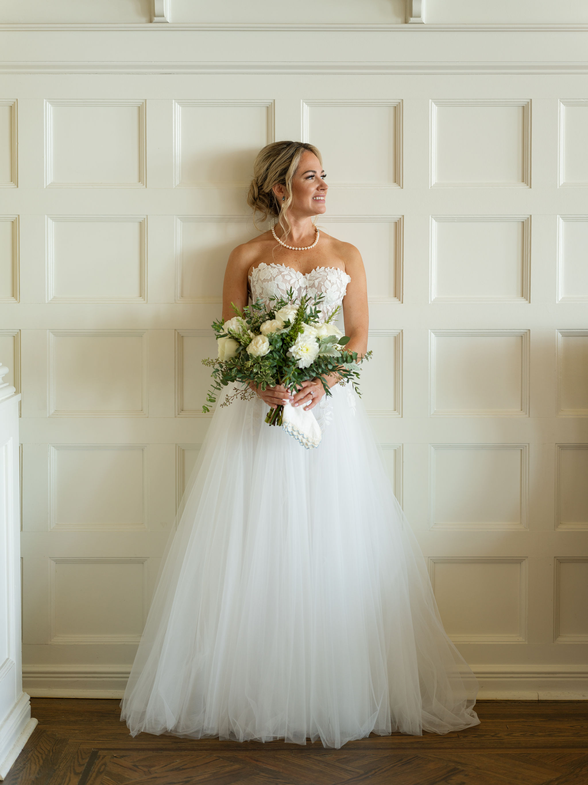 A bride with her bouquet standing in front of a white paneled wall at the Sagamore Resort.