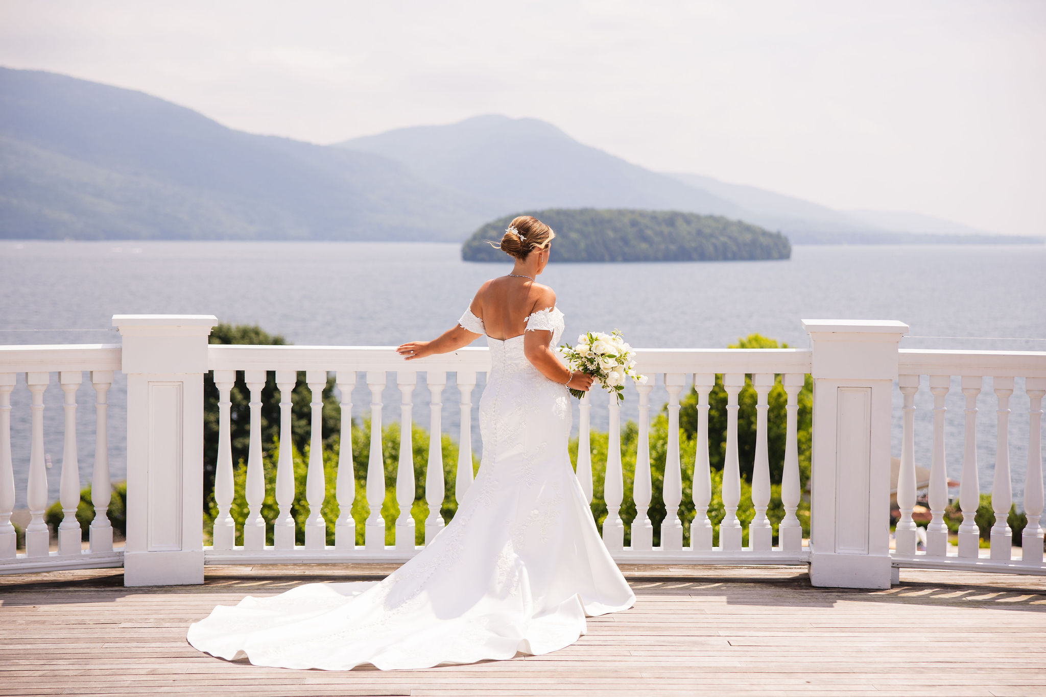 Bride with bouquet standing on upstairs balcony of Sagamore Resort, with Lake George and Dome Island in the background.