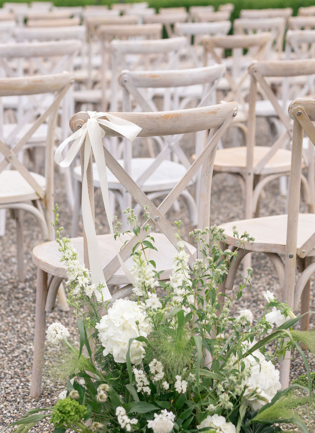 An aisle floral ground arrangement in white and green placed next to wedding guest chairs.